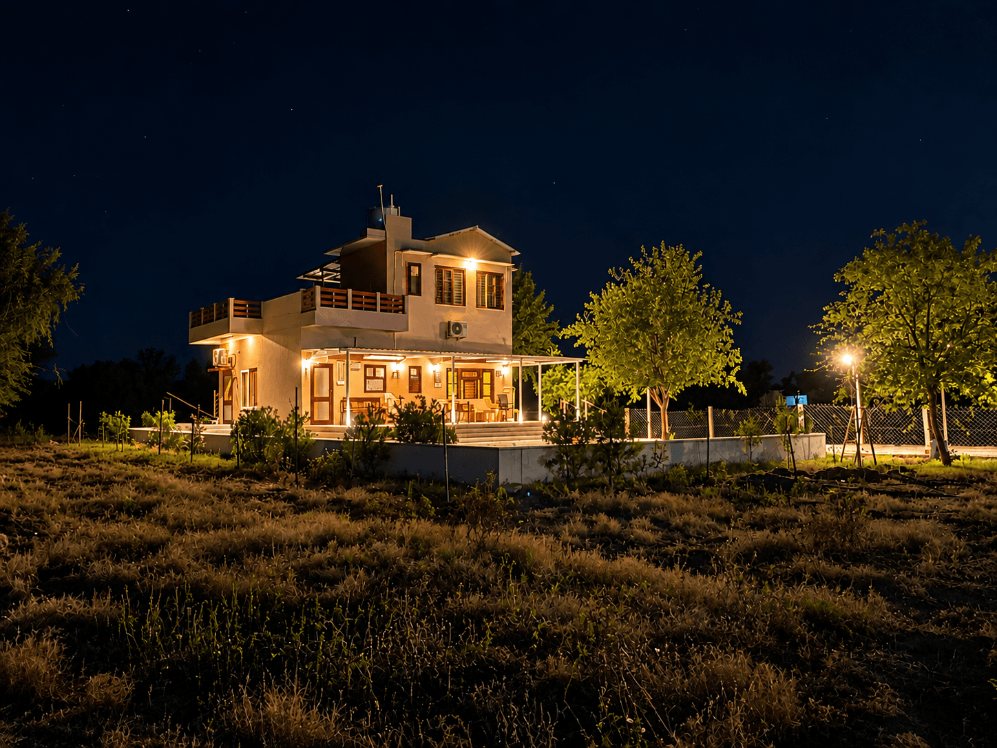 The Shiv Bagh farmhouse at night, lit warm across the open field